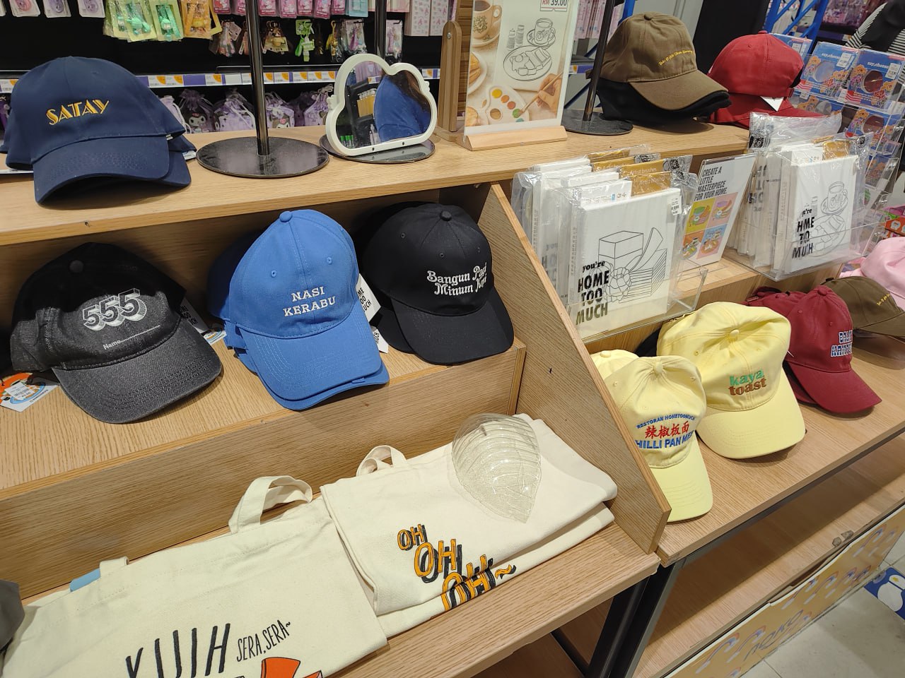 Полка с кепками, тканевыми сумками и канцелярскими товарами в магазине подарков или аксессуаров.