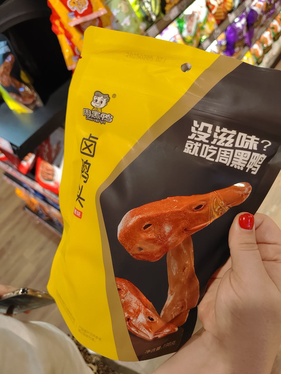 На изображении показан пакет с едой, который держит в руке женщина с красными ногтями. На пакете изображен гриб, а над ним написано на китайском языке. Пакет имеет желтый и черный цвет, и на нем написано "Mush