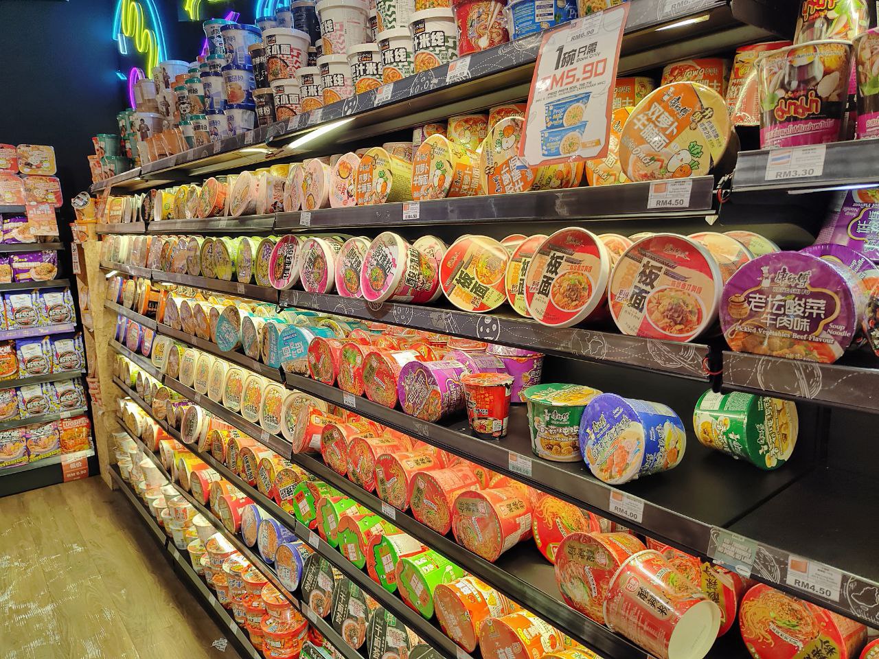 Это полка с различными видами супов в пластиковых контейнерах. На полке много разных видов супов, некоторые из них в пластиковых контейнерах, а другие в картонных коробках. На полке также есть несколько плакатов с ценами и информаци