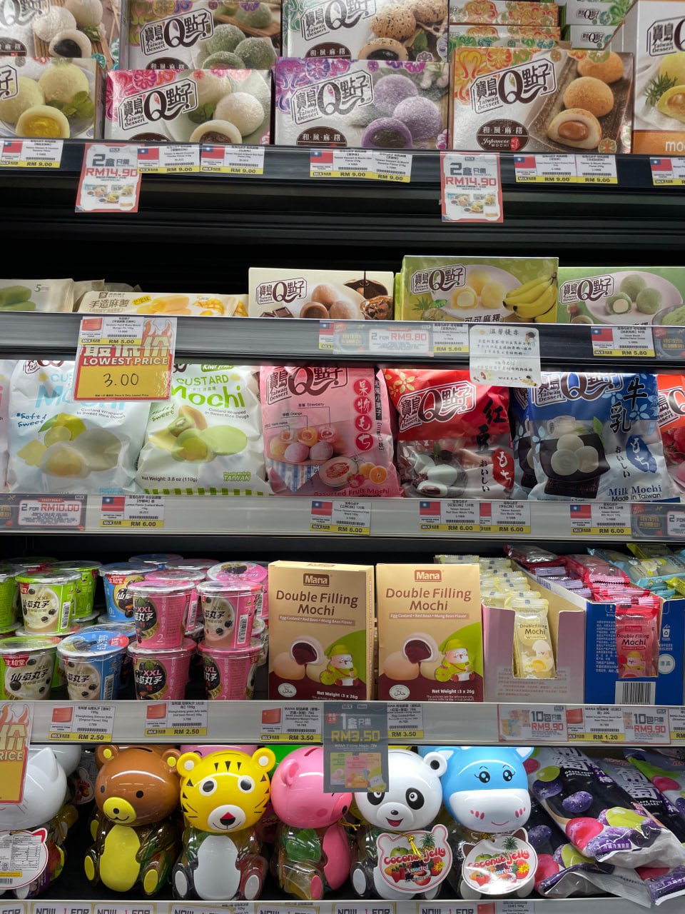 Это полка с продуктами в супермаркете. На полке много разных продуктов, в том числе конфеты, мороженое, йогурты, мучные изделия и другие. На полке также есть несколько игрушек в виде животных. На полке есть