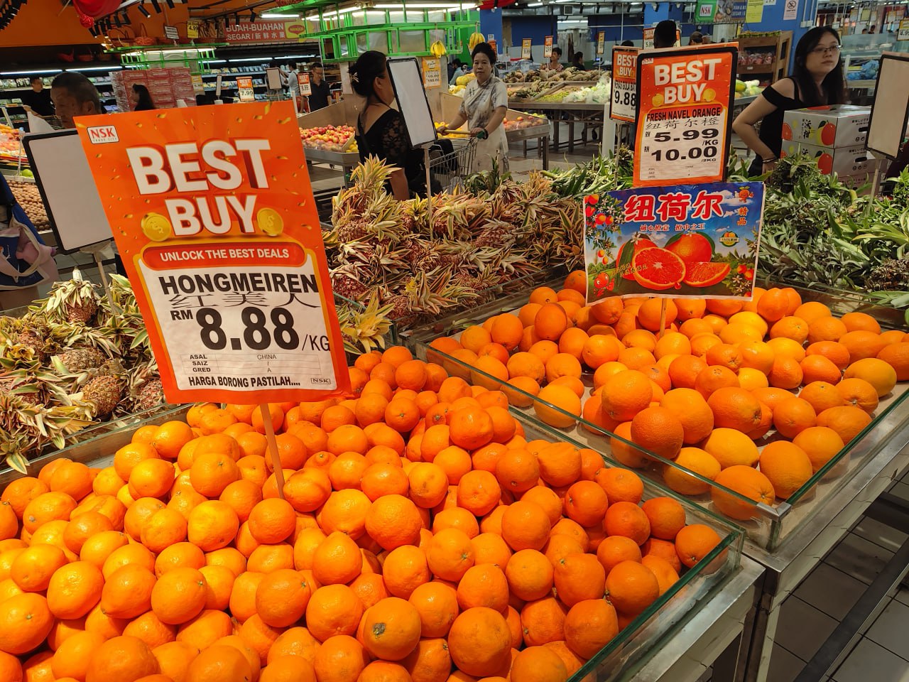 На изображении представлены два стола с апельсинами, на которых стоят две таблички с надписью "BEST BUY" и цифрой "8.88" в центре. В левом верхнем углу на одной из табличек написано "UNLOCK THE