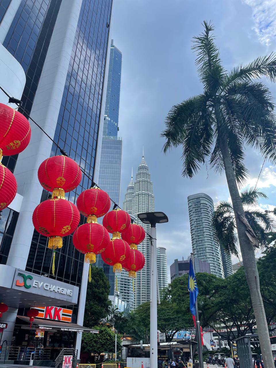 На изображении видны красные китайские фонарики, висящие над улицей, и несколько высоких зданий, расположенных в центре города. В центре изображения видны два высоких здания, одно из которых имеет форму конуса, а другое -